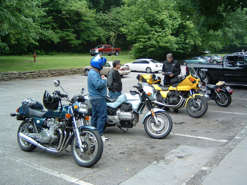 Four motorcycles parked in a lot with people standing around them