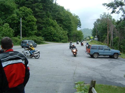 1985 Ford LTD Crown Victoria - Motorcycles and a blue SUV are stopped on a road surrounded by trees.