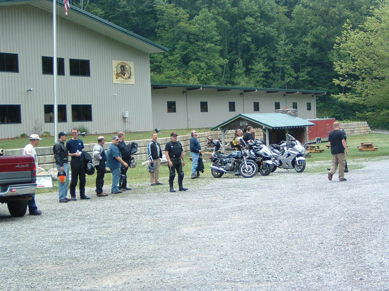Several motorcycles parked in a gravel lot near a building