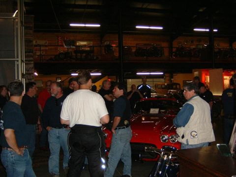 1985 Ford LTD Crown Victoria - A group of people are looking at a red sports car inside a building with multiple levels.