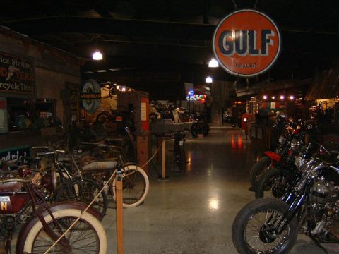 1985 Ford LTD Crown Victoria - A collection of vintage motorcycles and advertising signs are displayed inside a dimly lit museum.