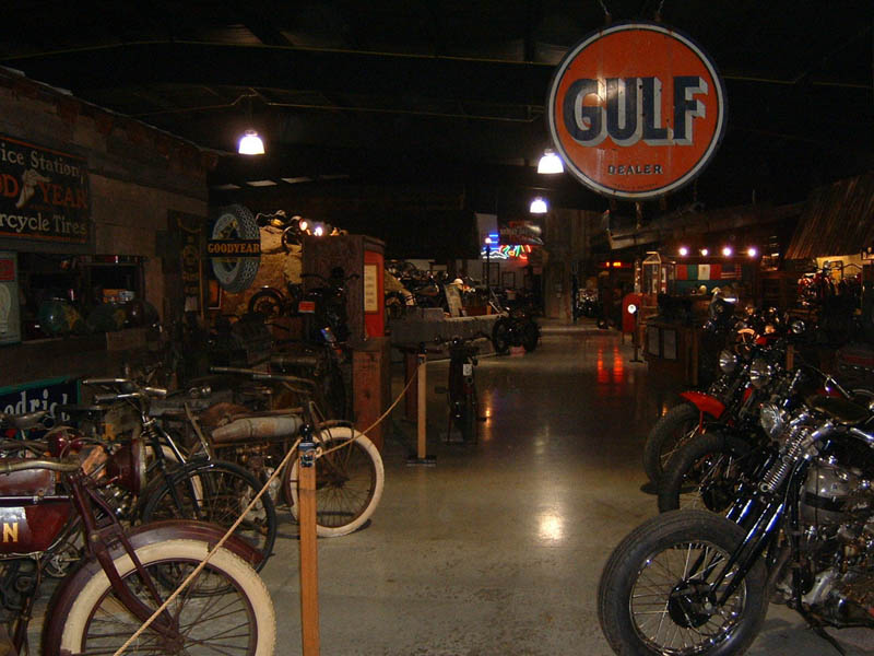 Interior of a museum with multiple vintage motorcycles and signs, including a Gulf Dealer sign