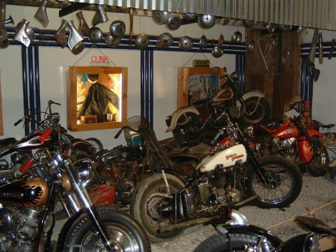 1985 Ford LTD Crown Victoria - A display of multiple vintage motorcycles, some Harley-Davidson branding, are arranged in a room with various motorcycle parts on the wall.