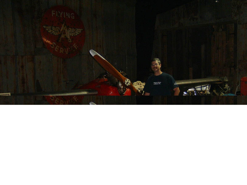 Red airplane with wooden propeller and a man standing next to it