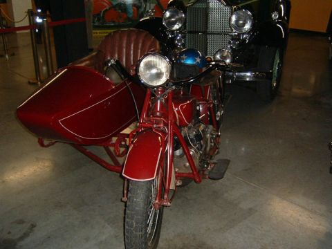 1985 Ford LTD Crown Victoria - A vintage motorcycle with a sidecar is parked indoors, with a classic car visible behind it.