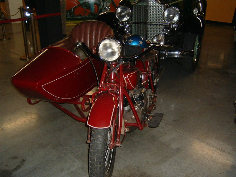 Red motorcycle with sidecar, front view. Vintage car in background
