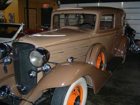 1985 Ford LTD Crown Victoria - A vintage tan sedan with distinctive orange wheels is displayed indoors.
