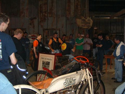 1985 Ford LTD Crown Victoria - A group of people observe vintage motorcycles in a workshop setting.
