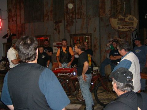 1985 Ford LTD Crown Victoria - A group of people admire a vintage red motorcycle inside a building with Harley-Davidson signage.