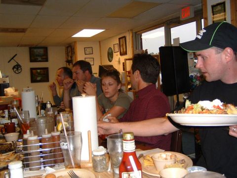 1985 Ford LTD Crown Victoria - A group of people are gathered around a table in a casual dining establishment, enjoying a meal together.