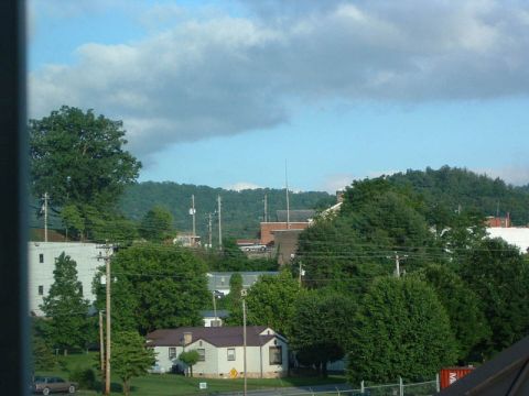 1985 Ford LTD Crown Victoria - A lone sedan is visible in this daytime scene of a residential area with trees and buildings.