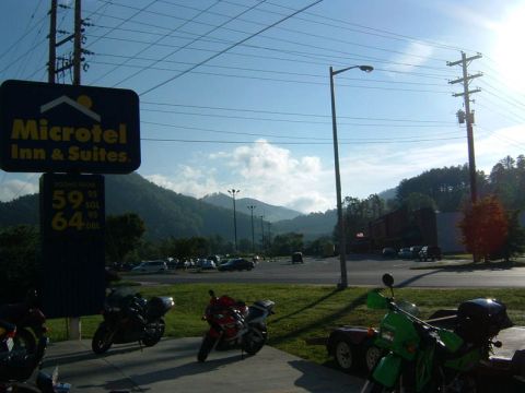 1985 Ford LTD Crown Victoria - Several motorcycles are parked outside a Microtel Inn & Suites, with a scenic mountain backdrop under a bright sky.
