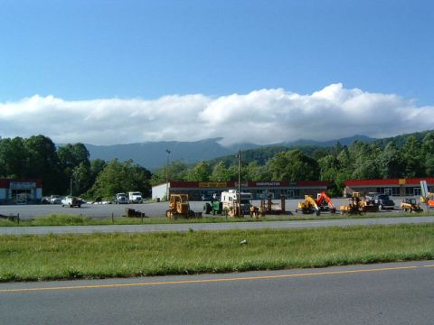 1985 Ford LTD Crown Victoria - A variety of construction vehicles are parked outside businesses with a mountain range visible in the distance.