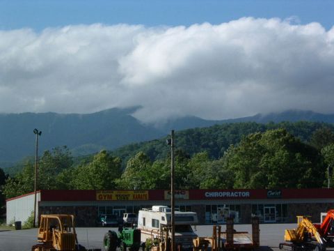 1985 Ford LTD Crown Victoria - Various vehicles and construction equipment are parked in front of a commercial building with a mountainous backdrop.