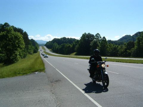 1985 Ford LTD Crown Victoria - A motorcycle rider cruises down a scenic highway on a sunny day.