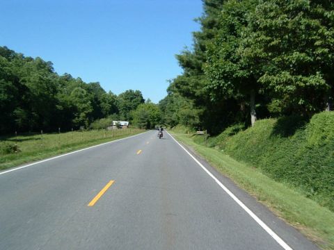 1985 Ford LTD Crown Victoria - A motorcycle travels down a rural highway on a clear day.