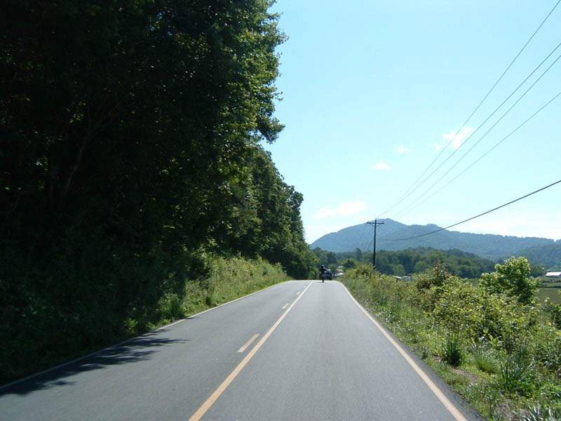 Motorcycle on a two-lane road with trees and mountains in the background