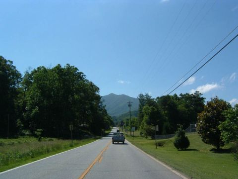 1985 Ford LTD Crown Victoria - A truck drives down a rural road with trees and mountains in the background under a clear blue sky.