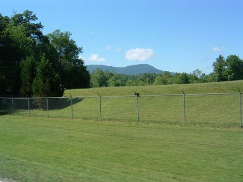 1985 Ford LTD Crown Victoria - A wide shot of a rural landscape with a fence in the foreground and rolling hills and mountains in the distance.