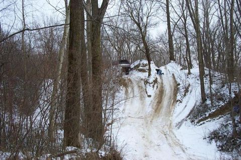 1992 Ford Bronco - A dark SUV navigates a snowy, off-road hill with a person sliding down nearby.