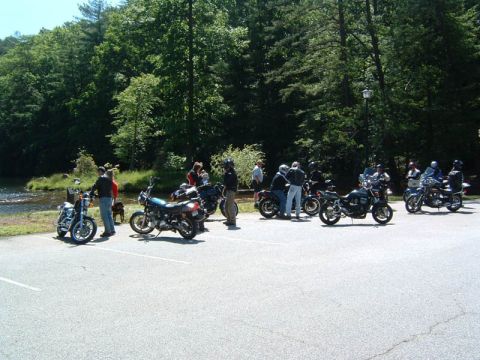 1985 Ford LTD Crown Victoria - A group of motorcyclists and their bikes are gathered in a scenic spot by the water, enjoying a sunny day.