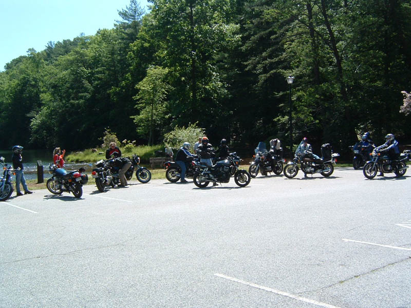 Group of motorcycles parked in a lot with trees and water in the background