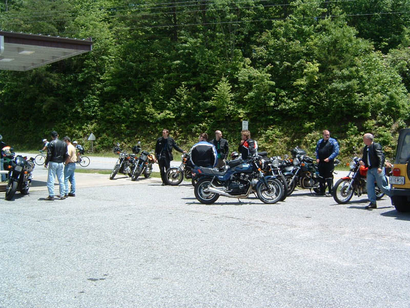 Group of motorcycles parked near a gas station with people standing around