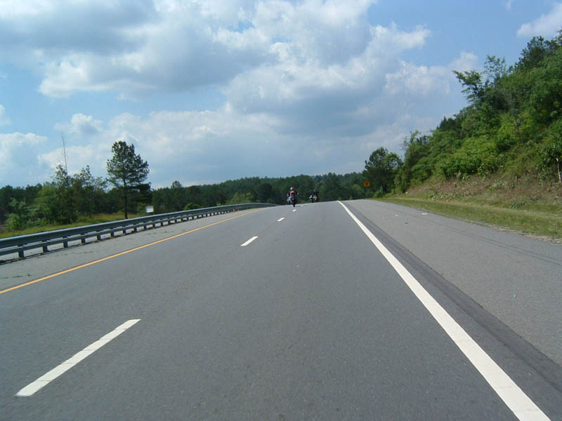 Two motorcycles ride on a highway under a cloudy sky