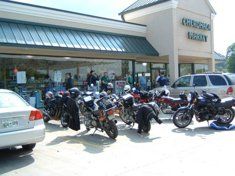 1985 Ford LTD Crown Victoria - Motorcycles are parked in front of the Cherokee Market, with people standing inside and outside the store.