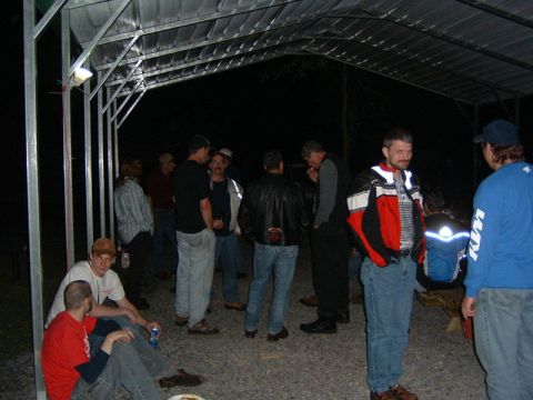 1985 Ford LTD Crown Victoria - A group of people are socializing under a covered area at night.