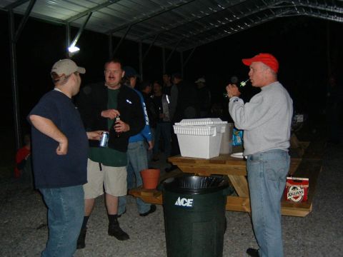 1985 Ford LTD Crown Victoria - An outdoor gathering takes place at night under a covered structure, with several people interacting.
