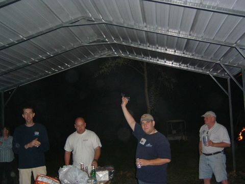 1985 Ford LTD Crown Victoria - People gathered under a metal carport at night, with a table of food and drinks in the foreground.