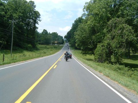 1985 Ford LTD Crown Victoria - Several motorcycles and a car travel down a highway surrounded by trees and green fields.