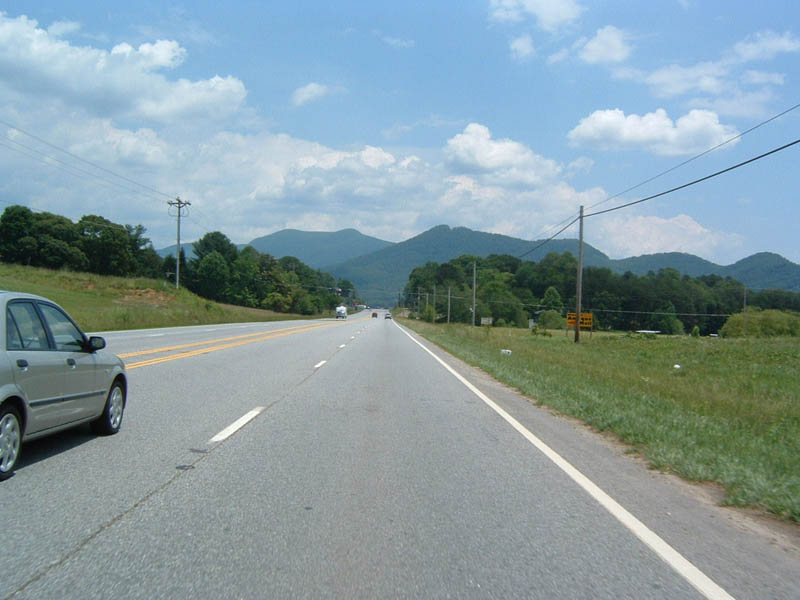 Silver sedan in the left lane of a two-lane highway, mountains in the distance