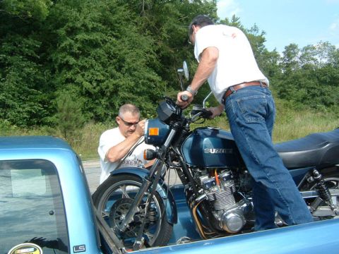 1985 Ford LTD Crown Victoria - Two men load a blue Suzuki motorcycle into the bed of a blue pickup truck.