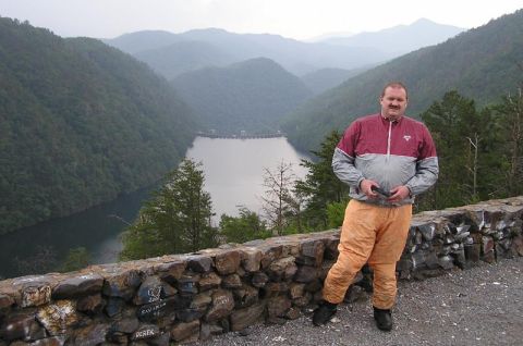 1985 Ford LTD Crown Victoria - A man poses for a photo on a stone wall with a scenic view of a dam and a valley in the background.