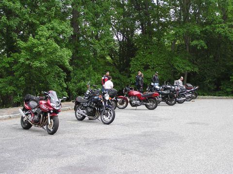1985 Ford LTD Crown Victoria - A group of motorcycles are parked in an outdoor lot, with people standing around them.