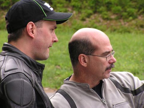 1985 Ford LTD Crown Victoria - Two men in motorcycle jackets are seen outdoors, with one wearing a black baseball cap and the other wearing glasses.