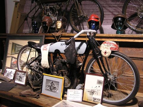 1985 Ford LTD Crown Victoria - A vintage Harley-Davidson motorcycle is displayed with historical memorabilia, including helmets and framed photographs.