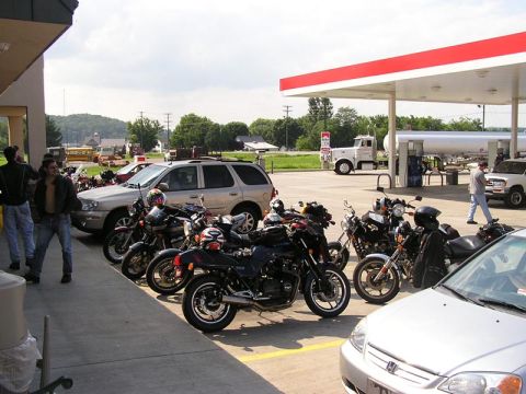 1985 Ford LTD Crown Victoria - Motorcycles and cars are parked at a gas station under a red and white canopy.