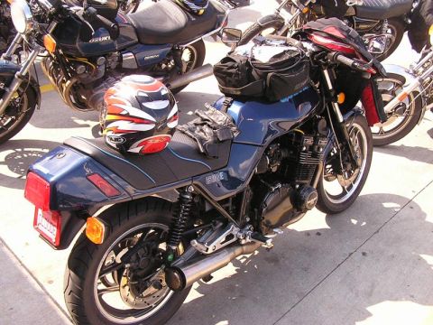 1985 Ford LTD Crown Victoria - A dark blue motorcycle is parked with other bikes, a helmet and gloves on the seat.