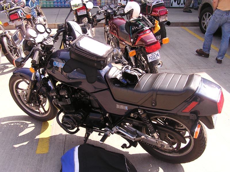 Dark gray Suzuki GS1000E motorcycle side view with tank bag and other motorcycles in background