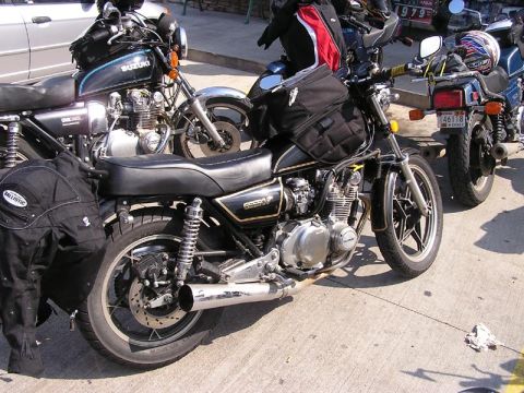 1985 Ford LTD Crown Victoria - Motorcycles are parked on a paved surface, with one black motorcycle in the foreground and a Suzuki in the background.