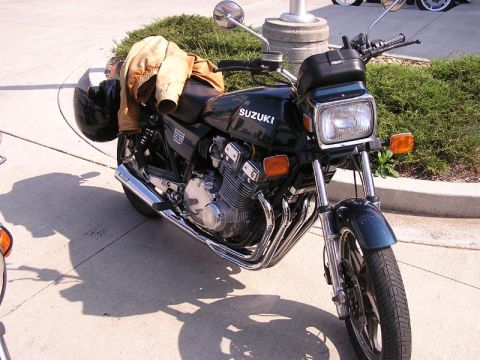 1985 Ford LTD Crown Victoria - A black Suzuki motorcycle is parked on a concrete surface with a jacket and helmet on the seat.