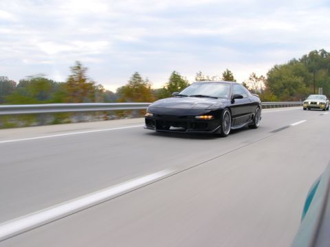 1997 Ford Probe - A black coupe with an aggressive body kit drives down a highway under a cloudy sky.