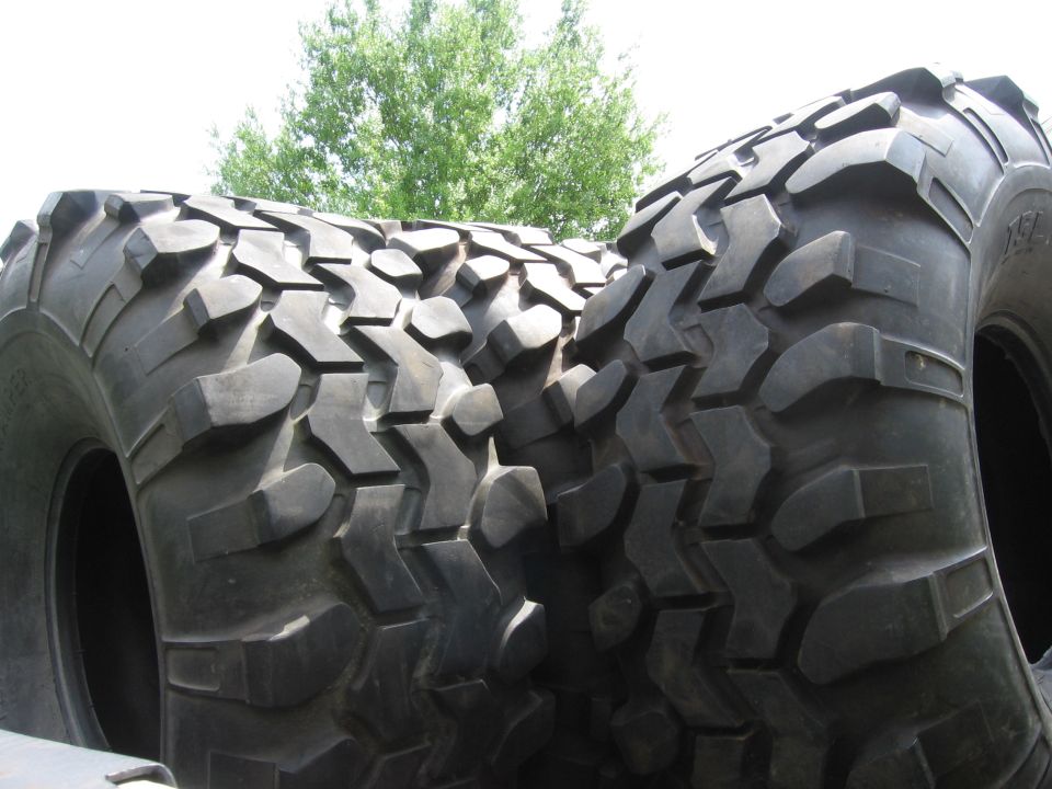 Two large, knobby off-road tires stacked, with trees in the background
