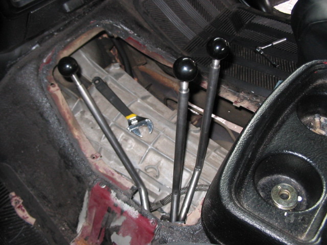 Interior shot of a vehicle's manual transmission area with three shifters and a wrench on the transmission housing