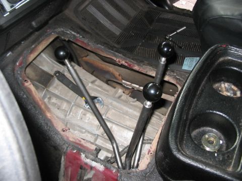 1991 Ford Bronco - The interior of a vehicle displays a transmission tunnel with multiple manual shifters and a wrench, with visible red paint beneath the tri…