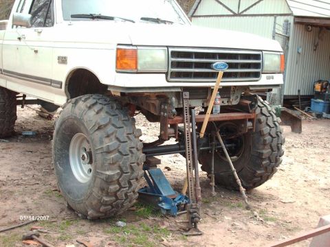 1990 Ford F-150 - A white Ford truck is shown with its front end lifted on jacks, oversized tires and modifications.