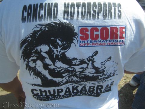 1990 Ford Bronco - back of a white T-shirt reads Cancino Motorsports and Chupakabras Off-Road Racing with a SCORE International logo and creature artwork.